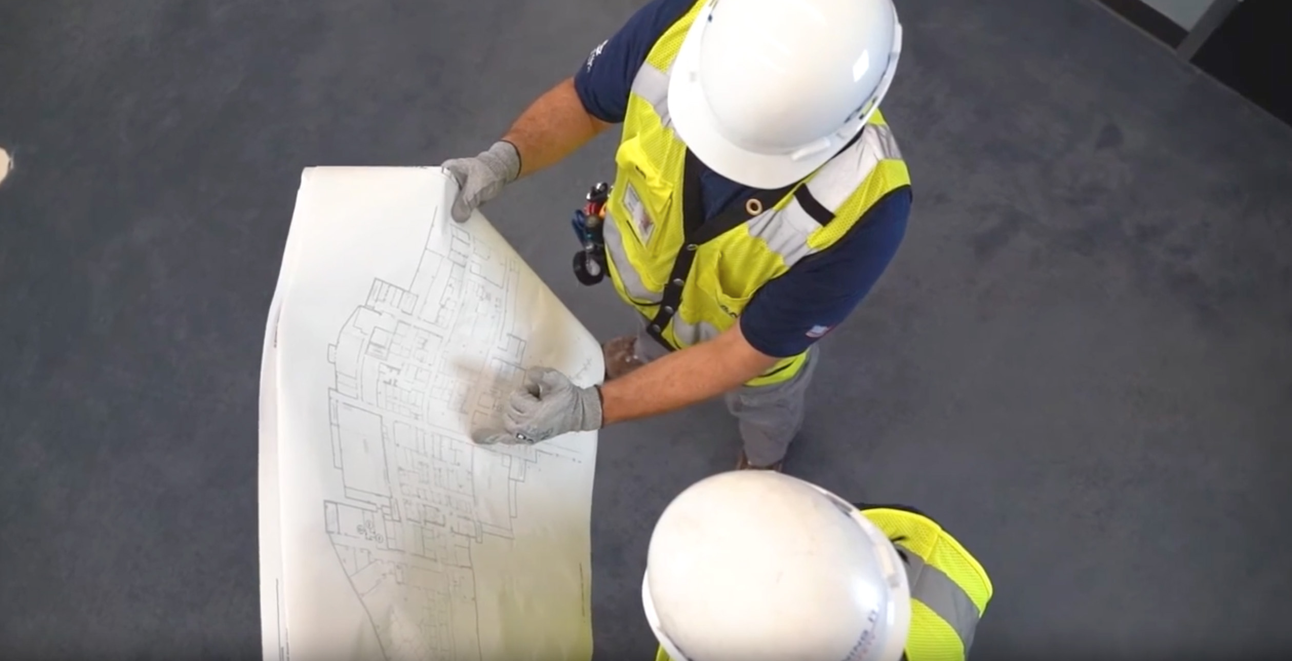 Workers in hard hats and safety vests reviewing a blueprint schematic.